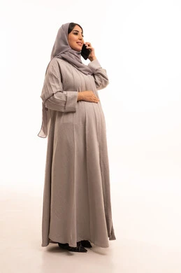 دمج التقنية والتكنولوجيا في الحياة اليومية، التواصل مع الاهل والاصدقاء، بورترية من الجانب لامراه عربيه خليجيه سعودية حامل ترتدي العباءة و الحجاب تقوم بأجراء مكالمة هاتفية باستخدام الجوال، دردشة ومحادثات وتعارف، الجسم بالطول الكامل، خلفية بيضاء