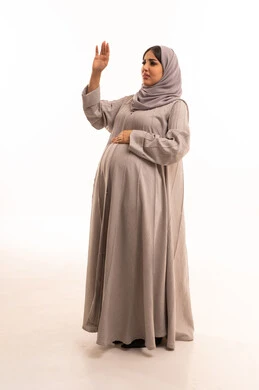 Expressions of rejection and refusal, the command to stop doing something, a side portrait of a pregnant Arab Gulf Saudi woman wearing an abaya and hijab raising her hands in gestures indicating prohibition, feelings of discomfort and anger, full-body, white background.