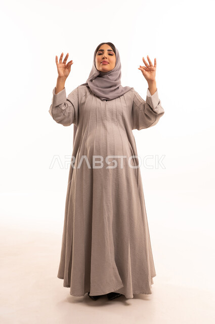 A symbol of quality and excellence, expressions of joy and happiness, a portrait of a pregnant Arab Gulf Saudi woman wearing an abaya and hijab, raising her hands with gestures indicating admiration and satisfaction, the concept of acceptance and agreement, a full-body image, white background.