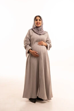 The concept of pregnancy and childbirth, a portrait of a pregnant Saudi Arabian Gulf woman wearing an abaya and hijab, placing her hand on her belly, looking at the camera with gestures of joy, expressions of excitement and longing for the arrival of the newborn, concern for the health of the fetus, full-body image, white background.