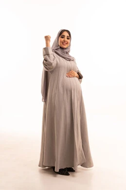 Expressions of joy and happiness, success and achieving goals, a portrait of a pregnant Arab Gulf Saudi woman wearing an abaya and hijab looking at the camera with facial and hand gestures indicating victory and triumph, full body, white background.
