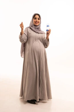 Caring for children's health and well-being, providing the necessary tools for child care, expressions of success and achieving goals, paying attention to the nutrition and growth of children, a portrait of a pregnant Saudi Gulf Arab woman wearing an abaya and hijab holding a baby bottle in her hands, full-body, white background.