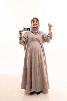 Success and achieving goals, the concept of pregnancy and childbirth, using ultrasound to reassure about the baby, a portrait of a pregnant Saudi Gulf Arab woman wearing an abaya and hijab holding the ultrasound and raising her hands in gestures of excitement, full-body, white background.
