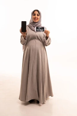 A blank black screen display, the concept of pregnancy and childbirth, using ultrasound to check on the baby, a portrait of a pregnant Arab Gulf Saudi woman wearing an abaya and hijab holding a mobile phone and ultrasound images in her hands, full-body, white background.