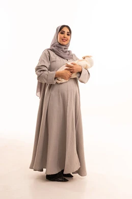 إيماءات الاهتمام والحب، الشعور بالأمان في حضن الامهات، بورتريه لامرأة عربية خليجية سعودية حامل ترتدي العباءة و الحجاب تحمل صغيرتها بعطف وعناية، مفهوم عاطفة الأمومة وأهميتها للطفل، تعزيز وتمكين الروابط الأسرية، الجسم بالطول الكامل، خلفية بيضاء