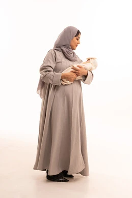 The feeling of safety in the embrace of mothers, gestures of care and love, a portrait of a pregnant Saudi Gulf Arab woman wearing an abaya and hijab, holding her little one with affection and care, the concept of maternal emotion and its importance to the child, strengthening and empowering family bonds, full-body, white background.