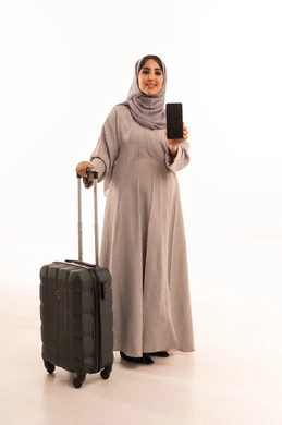 عرض شاشة سوداء فارغه ، تصفح الانترنت ومواقع التواصل الاجتماعي، رحلات جوية سياحية، الدردشة مع الأهل والأصدقاء عبر الموبايل, بورتريه لامرأة عربية خليجية سعودية حامل ترتدي العباءة و الحجاب تمسك بيديها حقيبة السفر و الهاتف المحمول،الجسم بالطول الكامل، خلفية بيضاء