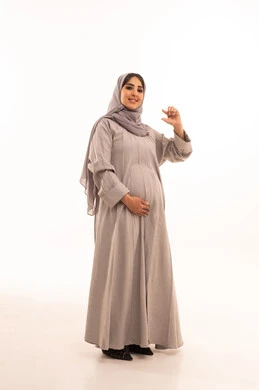 محاولة الإحاطة والإمساك بشيء ما، بورتريه لامرأة عربية خليجية سعودية حامل ترتدي العباءة و الحجاب تقوم بتحجيم عنصر صغير، صورة الجسم بالطول الكامل، خلفية بيضاء