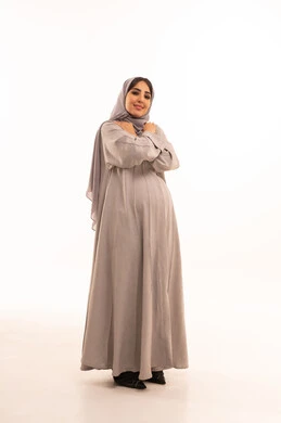 الشعور بالصقيع والقشعريرة والتجمد، الاستمتاع بالأجواء الشتوية الثلجية الباردة، بورتريه لامرأة عربية خليجية سعودية حامل ترتدي العباءة و الحجاب تقوم باحتضان نفسها، النظر بإيماءات تدل على الاحساس بالبرد الشديد، موسم تساقط الثلج، الجسم بالطول الكامل، خلفية بيضاء