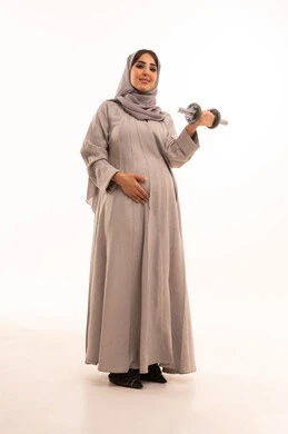 Weightlifting is a sports activity to maintain body health, burn fat and calories. A portrait of a pregnant Arab Gulf Saudi woman wearing an abaya and hijab doing weightlifting exercises (dumbbells), showing gestures of enthusiasm, joy, and readiness to exercise, full-body shot, white background.