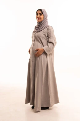 الجمال والاهتمام بالمظهر الخارجي، مفهوم الأنوثة والنعومة، بورتريه لامرأة عربية خليجية سعودية حامل ترتدي العباءة و الحجاب تقف باستقامة بتعابير الثقة بالنفس، النظر إلى الكاميرا بإيماءات السرور والسعادة، الجسم بالطول الكامل، خلفية بيضاء