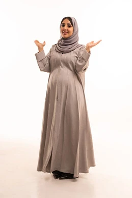 مفهوم الأنوثة والنعومة، النظر إلى الكاميرا بتعابير الفرح بحدوث أمر ما، بورتريه لامرأة عربية خليجية سعودية حامل ترتدي العباءة و الحجاب ترفع يديها إلى الأعلى بإيماءات السرور والسعادة، الجمال والاهتمام بالمظهر الخارجي، الجسم بالطول الكامل، خلفية بيضاء