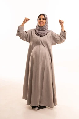 Success and achieving goals, the concept of joy in victory and winning, expressions of joy and happiness, a portrait of a pregnant Arab Gulf Saudi woman wearing an abaya and hijab raising her hands in gestures of enthusiasm, full-body, white background.