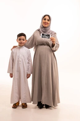 أهمية دور الأم في العناية بأولادها، بورترية لامراه عربيه خليجيه سعودية حامل ترتدي الحجاب و العباءة تقف برفقة ابنها تمسك بيديها اشعه السونار، مفهوم الحمل والانجاب، استخدام السونار للاطمئنان على الطفل، الجسم بالطول الكامل، خلفية بيضاء