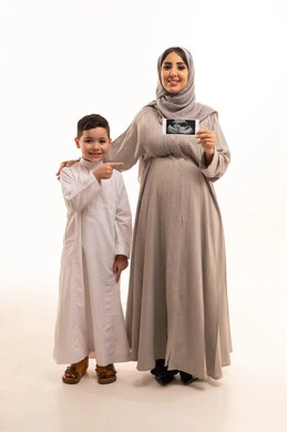 Monitoring pregnancy and ultrasound examination of the fetus, the concept of emotion in mothers, a portrait of an Arab Gulf Saudi pregnant woman holding the ultrasound image with her son, full-body, white background.