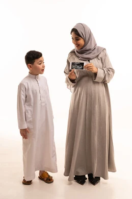 استخدام تقنية الموجات الصوتية لمتابعة صحة الطفل، مفهوم العاطفة عند الأمهات،  بورترية لامراه حامل عربيه خليجيه سعودية تمسك الاشعه الفوق صوتية برفقة ابنها، الجسم بالطول الكامل، خلفية بيضاء