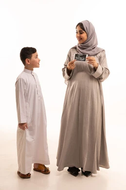 التأكد من سلامة الجنين عبر الفحص بالموجات الصوتية، مفهوم العاطفة عند الأمهات،  بورترية لامراه حامل عربيه خليجيه سعودية تمسك الاشعه الفوق صوتية برفقة ابنها، الجسم بالطول الكامل، خلفية بيضاء