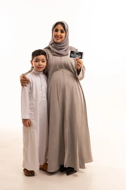 الاطمئنان على مراحل نمو الجنين باستخدام الأشعة فوق الصوتية، مفهوم العاطفة عند الأمهات،  بورترية لامراه حامل عربيه خليجيه سعودية تمسك الاشعه الفوق صوتية برفقة ابنها، الجسم بالطول الكامل، خلفية بيضاء