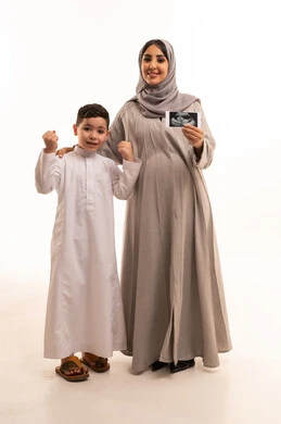 متابعة تطور الحمل والجنين من خلال فحص السونار، مفهوم الحمل و الانجاب، تعابير النجاح و تحقيق الهدف ،  بورترية لامراه حامل عربيه خليجيه سعودية تمسك الاشعه الفوق صوتية برفقة ابنها، الجسم بالطول الكامل، خلفية بيضاء