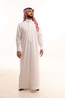 الأناقة والاهتمام بالمظهر الخارجي، النظر الى شيء ما ، مفهوم الرجولة والثقة بالنفس، بورتريه لرجل عربي خليجي سعودي يرتدي الشماغ والزي التقليدي يقف باستقامه و اعتدال ، الجسم بالطول الكامل، خلفية بيضاء