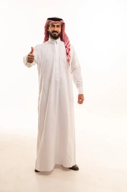 نظرات الحماس والشعور بالرضى, بورتريه لرجل عربي خليجي سعودي يرتدي الثوب والشماغ التقليدي يرفع إبهامه للأعلى بعلامة الجودة, الوقوف باستقامة والنظر إلى الكاميرا بإيماءات التفاعل والموافقة, صورة الجسم بالطول الكامل, خلفية بيضاء
