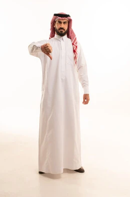 الشعور بالانزعاج من شيء ما، حركات يدين تدل على الرفض وعدم القبول والفشل، بورتريه لرجل عربي خليجي سعودي يرتدي الثوب التقليدي والشماغ يشير بإصبعه الابهام الى الأسفل بإيماءات عدم الاعجاب والتقييم السلبي، الطول الكامل للجسم, خلفية بيضاء