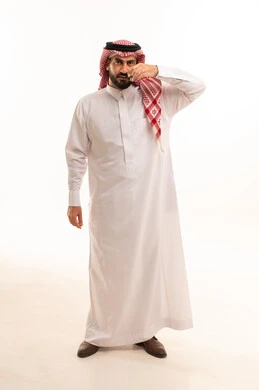 مركز تجميلي رجالي، استخدام المقص في العناية الشخصية، مفهوم الاهتمام بالجمال والمظهر الخارجي، بورتريه لرجل عربي خليجي سعودي يرتدي الثوب الابيض و الشماغ يقوم بقص و تصفيف الذقن والشارب ، الجسم بالطول الكامل، خلفية بيضاء