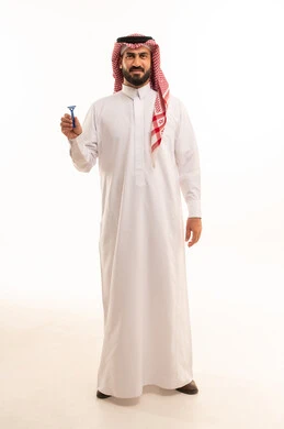 Looking at the camera with gestures of happiness and joy, maintaining elegance and personal hygiene, taking care of the skin and paying attention to the external appearance, a portrait of a Saudi Arabian Gulf man wearing traditional attire and a ghutrah holding a men's razor in his hand, full-body shot, white background.
