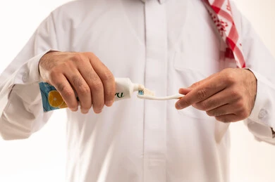 Daily oral and dental hygiene, a close-up portrait of a Saudi Arabian Gulf man wearing a white thobe and a ghutrah, brushing his teeth with a toothbrush and toothpaste, avoiding tooth decay and gum diseases, white background.