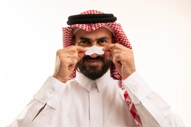التخلص من الرؤوس السوداء والجلد الميت، مفهوم العناية بالنفس، العناية والاهتمام بنضارة وتحسين البشرة، بورترية مقرب لرجل عربي خليجي سعودي يرتدي الثوب الابيض و الشماغ يقوم بوضع لصقات الأنف، استخدام ماسكات تنظيف المسام ومكونات تجميلية، خلفية بيضاء