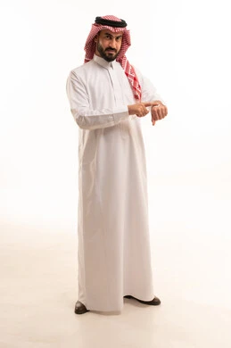 Moisturizing, cleansing, and brightening the skin, skincare routine, the concept of caring for and improving skin freshness, using youthful cosmetic ingredients, a portrait of a Saudi Arabian Gulf man wearing a white thobe and shemagh applying moisturizer to his hands, full-body, white background.