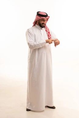 روتين العناية بالبشرة ، ترطيب وتنظيف وتفتيح الجلد، مفهوم الإهتمام بنضارة وتحسين البشرة، استخدام مكونات تجميلية شبابية، بورتريه لرجل عربي خليجي سعودي يرتدي الثوب الابيض و الشماغ يضع كريم المرطب على يديه ، الجسم بالطول الكامل، خلفية بيضاء