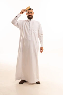 العناية الشخصية والاهتمام بالأناقة والجمال، تعابير وإيماءات تدل على السعادة والسرور، بورتريه دلرجل عربي خليجي سعودي يرتدي الثوب الابيض يقوم بتصفيف شعره باستخدام فرشاة الشعر ( المشط )، الجسم بالطول الكامل، خلفية بيضاء