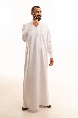 مفهوم العناية والاهتمام بالجمال والأناقة والمظهر الخارجي، بورتريه لرجل عربي خليجي سعودي يرتدي الثوب الابيض يقوم بتمشيط ذقنه باستخدام ( المشط )، تعابير وإيماءات تدل على السعادة والسرور، الجسم بالطول الكامل، خلفية بيضاء