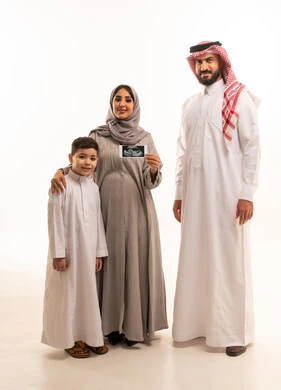 مفهوم الحمل و الانجاب، إجراء فحص دوري للجنين باستخدام الأشعة الصوتية، بورترية لامراة حامل عربيه خليجيه سعودية ترتدي العباءة و الحجاب تحمل بيديها اشعه السونار برفقة ابنها و زوجها، الجسم بالطول الكامل، خلفية بيضاء