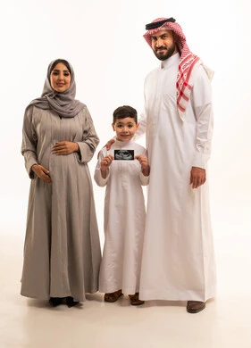 استخدام الأشعة فوق الصوتية لمتابعة الحمل، النظر للكاميرا بتعابير السعادة و السرور، الترابط الأسري والعاطفة بين أفراد العائلة، بورترية لولد عربي خليجي سعودي يرتدي الثوب الابيض يمسك بيديه اشعه السونار برفقة والدية ، الجسم بالطول الكامل، خلفية بيضاء