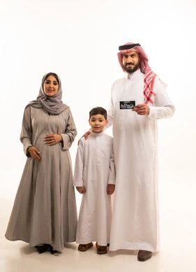 Looking at the camera with expressions of happiness and joy, family bonding and affection among family members, the concept of pregnancy and childbirth, an Arab Gulf Saudi man wearing a white thobe and a ghutrah holding a sonogram in his hands accompanied by his wife and son, full-body shot, white background.
