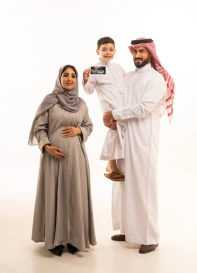 Family bonding and emotions among family members, looking at the camera with expressions of happiness and joy, using ultrasound to monitor pregnancy, a portrait of an Arab Gulf Saudi boy wearing a white thobe holding a sonogram in his hands accompanied by his parents, full-body, white background.
