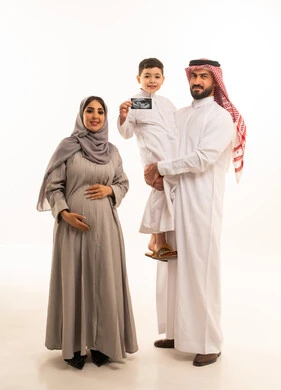 النظر للكاميرا بتعابير السعادة و السرور، الترابط الأسري والعاطفة بين أفراد العائلة، استخدام الأشعة فوق الصوتية لمتابعة الحمل، بورترية لولد عربي خليجي سعودي يرتدي الثوب الابيض يمسك بيديه اشعه السونار برفقة والدية ، الجسم بالطول الكامل، خلفية بيضاء