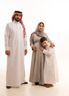 الشوق والارتباط بالجنين القادم، بورترية لولد عربي خليجي سعودي يرتدي الثوب الابيض يضع رأسه على بطن والدته برفقة ابيه ، مفهوم الترابط الأسري ، ايماءات السعادة و السرور، الجسم بالطول الكامل، خلفية بيضاء