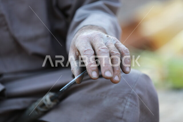 مزارع عربي خليجي يقوم بسن المنجل الزراعي ، اداة الحصاد ،ادوات قديمة تستخدم في الزراعة ، الزراعة في المملكة العربية السعودية