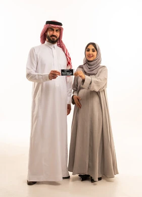 Checking the child's safety using ultrasound, a portrait of a Saudi Arabian Gulf man wearing a white thobe and a ghutrah holding a sonogram in his hands alongside his wife, the concept of pregnancy and childbirth, gestures of happiness and joy, full-body, white background.