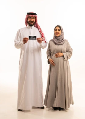 Monitoring the condition of the fetus through ultrasound examination, a portrait of a Saudi Arabian Gulf man wearing a white thobe and a ghutrah holding a sonogram in his hands alongside his wife, the concept of pregnancy and childbirth, gestures of happiness and joy, full-body, white background.