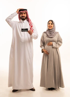 التذكر المفاجئ لشيء هام، فحص حالة الجنين بواسطة جهاز السونار،  بورترية لرجل عربي خليجي سعودي يرتدي الثوب الابيض و الشماغ يحمل اشعه السونار برفقه زوجته يضع يديه على رأسه ، الجسم بالطول الكامل، خلفية بيضاء