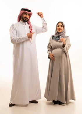 إجراء فحص السونار للاطمئنان على صحة الطفل، بورترية لامراه حامل عربيه خليجيه سعودية ترتدي العباءة و الحجاب تمسك بيديها اشعه السونار برفقه زوجها ، الاشارة بايماءات السعادة و السرور، الجسم بالطول الكامل، خلفية بيضاء