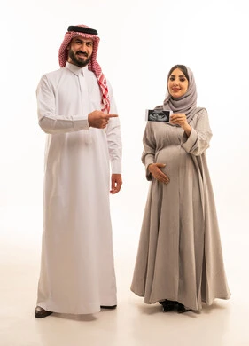 The use of ultrasound to monitor the fetus, a portrait of a pregnant Arab Gulf Saudi woman wearing an abaya and hijab holding a sonogram in her hands accompanied by her husband, signaling with gestures of happiness and joy, full-body, white background.