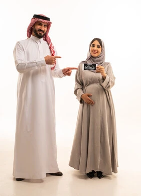 Monitoring the growth of the fetus through ultrasound, a portrait of a pregnant Arab Gulf Saudi woman wearing an abaya and hijab holding a sonogram in her hands accompanied by her husband, signaling with gestures of happiness and joy, full-body, white background.