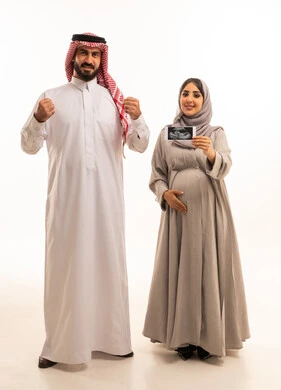 الاطمئنان على صحة الطفل، تعابير النجاح و تحقيق الاهداف، بورترية لامراه حامل عربيه خليجيه سعودية ترتدي العباءة و الحجاب تمسك بيديها اشعه السونار برفقه زوجها ، ايماءات السعادة و السرور، الجسم بالطول الكامل، خلفية بيضاء
