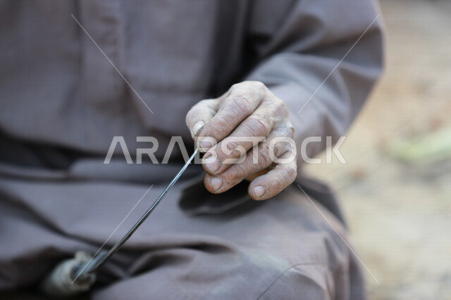 مزارع عربي خليجي يقوم بسن المنجل الزراعي ، اداة الحصاد ،ادوات قديمة تستخدم في الزراعة ، الزراعة في المملكة العربية السعودية