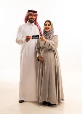 مفهوم الحمل والانجاب، الاهتمام بصحة الجنين ، بورترية لامراه حامل عربيه خليجيه سعودية ترتدي الحجاب و العباءة تقف برفقه زوجها يمسكان صورة الاشعه الفوق الصوتيه ، الاطمئنان على صحة الطفل، الجسم بالطول الكامل، خلفية بيضاء